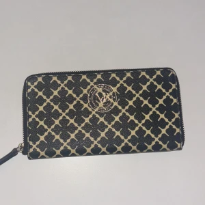 Mönstrad plånbok från By Malene Birger - Snygg plånbok från By Malene Birger med ett stilrent mönster i svart och beige. Plånboken har en praktisk dragkedja och flera fack för kort och kontanter. Perfekt accessoar för att hålla ordning på dina värdesaker.