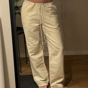 Beige linnebyxor med snörning - Snygga beige linnebyxor med avslappnad passform och snörning i midjan. Perfekta för en bekväm och stilren look. Byxorna har en rak och luftig stil som passar bra till varmare dagar.