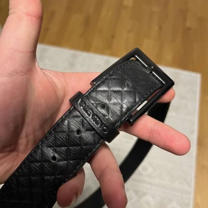 Svart bälte från Valentino - Snyggt svart bälte från Valentino med ett stilrent rutmönster. Tillverkat i skinn och har en klassisk spänne i svart. Perfekt för att ge en elegant touch till din outfit.