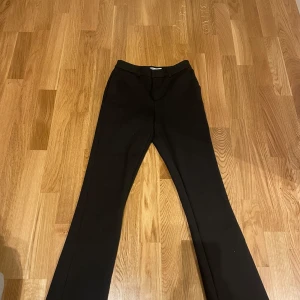 Svarta kostymbyxor - Snygga svarta kostymbyxor med en klassisk design. De har en rak passform och är perfekta för en stilren look. Byxorna har en dragkedja och knapp framtill med 2 fickor där bak