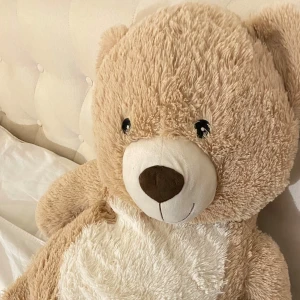 Stor beige nallebjörn - Säljer en stor och gosig nallebjörn i beige färg med vit mage. Perfekt för kramar och som dekoration i sovrummet. Den har en söt brun nos och svarta ögon som ger den ett vänligt uttryck. Haft den i ungefär 6 månader 