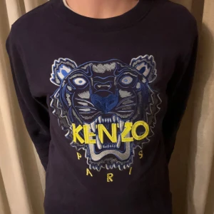 Svart tröja med tigerbroderi från Kenzo - Snygg svart tröja från Kenzo med ett stort, färgglatt tigerbroderi på framsidan. Tröjan har långa ärmar och en rund halsringning. Perfekt för en cool och avslappnad stil.