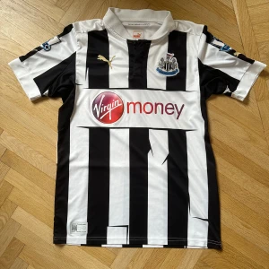 Svartvit randig fotbollströja från Puma - Säljer en klassisk svartvit randig fotbollströja från Puma med korta ärmar. Tröjan har ett tryck av Virgin Money på framsidan och Cisse nummer 9 på baksidan. 