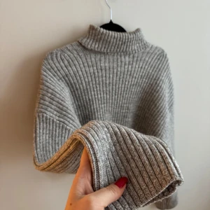 Grå ribbad polotröja - Säljer en mysig grå ribbad polotröja med långa ärmar. Perfekt för kyliga dagar och ger en stilren look. Tröjan har en hög krage som håller dig varm och bekväm. Passar bra till både jeans och kjol.