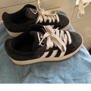 Svarta sneakers från Adidas campus  - Säljer ett par Adidas campus med vita ränder och snörning. Skorna har en vit sula och är perfekta för en avslappnad stil. storlek 37/36 inte använda så mycket skriv om fler bilder