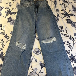 Blå jeans med slitningar - Snygga blå jeans från 157 med slitningar på knäna. De har en klassisk femficksdesign och knappgylf. Perfekta för en avslappnad stil.