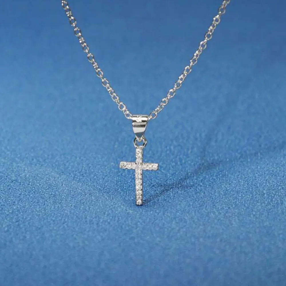 Elegant silverhalsband med ett glittrande korshänge. Hänget är dekorerat med små gnistrande stenar som ger en lyxig känsla. Perfekt för att lägga till en touch av elegans till din stil. 925 sterling silver (äkta silver). Asusteet.