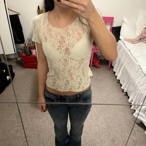 Vit spetsblus - Säljer en söt krämvit spetsblus med korta ärmar. Blusen har ett vackert blommigt mönster och är lätt genomskinlig.