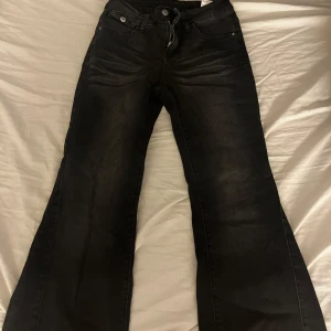 Svarta bootcut jeans - Snygga svarta bootcut jeans med hög midja. De har en klassisk femficksdesign och en knapp- och dragkedjestängning framtill. Perfekta för en stilren look.
