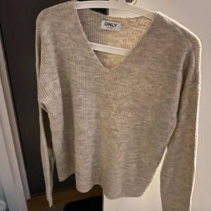 Beige stickad tröja från ONLY - Säljer en mysig beige stickad tröja från ONLY. Tröjan har en v-ringad hals och långa ärmar, perfekt för kyligare dagar. Den är enkel och stilren, vilket gör den lätt att matcha med olika outfits.
