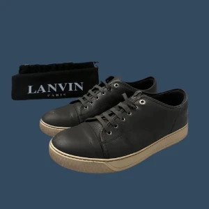 Lanvins grå - Säljer ett par stilrena svarta sneakers från Lanvin i mycket bra skick. Skorna har en klassisk design med snörning och en beige sula som ger en snygg kontrast. Perfekta för både vardag och festliga tillfällen. Kommer med dustbag. Gjorda i läder. Hör av er vid frågor ☺️ PRIS KAN DISKUTERAS.