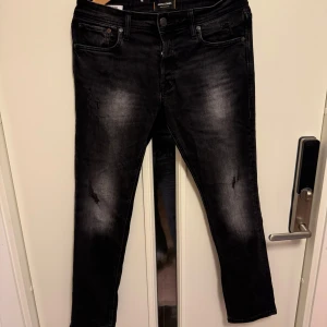 Svarta jeans från Jack & Jones - Säljer ett par svarta slim fit jeans från Jack & Jones i modellen Slim/Glenn i storlek 32/30. De är i bra skick med en snygg tvättad look och lätt slitna detaljer. Perfekta för både vardag och fest! Jag är 175-177 och väger 70kg