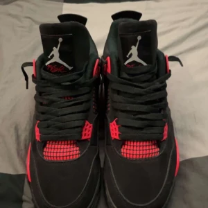 Svarta och röda Nike Air Jordans - Säljer ett par snygga Nike Air Jordans 4 i svart och rött. Skorna har en klassisk design med snörning och den ikoniska Jumpman-loggan. Perfekta för både vardag och fest. De är i mycket bra skick och redo för nya äventyr!