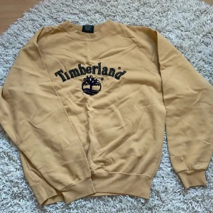 Gul sweatshirt från Timberland - Säljer en snygg gul sweatshirt från Timberland med deras ikoniska logga broderad på framsidan. Tröjan har långa ärmar och är perfekt för både höst och vår. Den är i bra skick och superbekväm att ha på sig. Perfekt för en avslappnad stil! 🌟