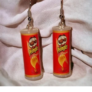 Pringles örhängen - Supercoola örhängen formade som Pringles-rör! De är i en härlig röd färg med den klassiska Pringles-loggan. Perfekta för att ge en rolig och unik touch till din outfit. Passar perfekt för fester eller när du vill sticka ut lite extra. Ett måste för alla snack-älskare! 🥳