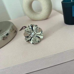 Silverfärgad blomring med pärldetalj - Säljer en unik och stilren ring i form av en blomma i silverfärg. Perfekt för att piffa upp vilken outfit som helst. Köpt från ett UF företag och säljer då jag har för många! Justerbar💓