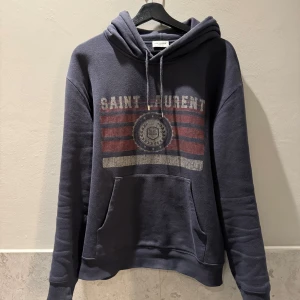 Saint Laurent hoodie - Säljer ett av de mest eftertraktade plaggen just nu, en mörkblå hoodie från Saint Laurent. Otroligt fint skick ingen defekt eller liknande. Storlek M/S, passar dig som är allt ifrån 175-183. För mer frågor är det bara att skriva!