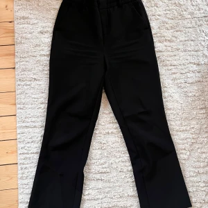 Svarta kostymbyxor från Gina Tricot - Snygga svarta kostymbyxor från Gina Tricot med hög midja och raka ben. Perfekta för en stilren look. Byxorna har hällor för bälte och diskreta fickor.