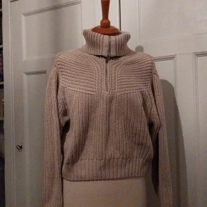 Beige stickad tröja från Gina Tricot - Säljer en mysig beige stickad tröja från Gina Tricot. Tröjan har en dragkedja framtill och en hög krage som kan vikas ner. Perfekt för kyliga dagar!