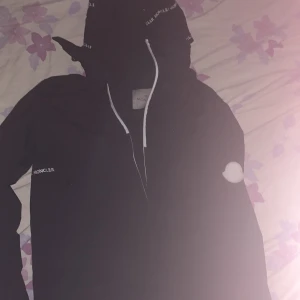 Svart jacka från Moncler - Säljer en snygg svart jacka från Moncler. Den har en huva med dragsko och Moncler-logga på bröstet. Perfekt för höst och vår. Jackan är i bra skick och passar både till vardags och fest.