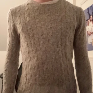Grå kabelstickad tröja från Ralph Lauren - Säljer en stilren grå kabelstickad tröja från Ralph Lauren. Tröjan har en klassisk design med rund hals och det ikoniska logotypbroderiet på bröstet. Perfekt för kyligare dagar. Dock ett litet hål i mitten men märks inte av vid användning. Ordinarie pris runt 1500 säljer för 449. Modellen är 175 ungefär.