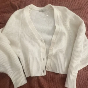 Vit ribbad kofta från Gina Tricot - Säljer en stilren vit kofta från Gina Tricot i premiumkvalitet. Koftan har en ribbad struktur och knappar framtill. Perfekt för lager-på-lager under kyligare dagar.