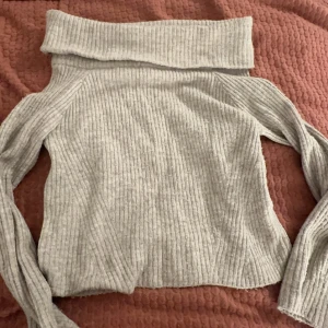 Grå ribbad polotröja från H&M - Säljer en mysig grå ribbad polotröja från H&M. Tröjan har en bred polokrage och långa ärmar, perfekt för kyliga dagar. Den är både stilren och bekväm, idealisk för höst och vinter.