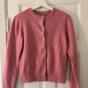 Rosa kofta från H&M - Säljer en söt rosa kofta från H&M i storlek XS. Koftan har långa ärmar och knappar framtill. Perfekt för att hålla sig varm och stilren under kyligare dagar. 💖