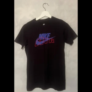 Svart Nike Air t-shirt - Säljer en svart Nike Air t-shirt i bomull med ett coolt tryck i blått och rött på framsidan. Perfekt för vardagsbruk eller träning. T-shirten är i bra skick. 