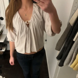 Vit/beige blus med trekvartsärm - Säljer en stilren vit/beige blus med trekvartsärm och en dekorativ knytning framtill. Blusen har en lös passform och är perfekt för både vardag och festliga tillfällen. Från zara i storlek S!🙌💕