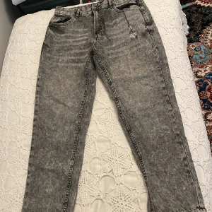 Grå jeans från FB Sister - Säljer ett par grå jeans från FB Sister i storlek XL. De har en cool, tvättad look och är i mom's fit-stil. Jeansen har slitna detaljer och en klassisk femficksdesign. Perfekta för en avslappnad vardagsstil!