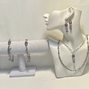 Smyckeset i silver och lilla Jewelry A.J.D.Y  - Ett elegant smyckeset med halsband, armband och örhängen i silverfärg. Setet har detaljer med rosa pärlor och små hjärtan. Perfekt för att ge en glittrig touch till din outfit. Passar både till vardag och festliga tillfällen.Ett par örhängen och ett par armband plus en halsband handgjorda mycket mycket fint nytt oanvänd 