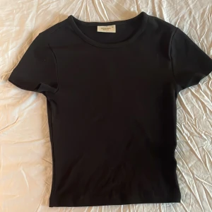 Svart t-shirt från Gina Tricot - Säljer en klassisk svart t-shirt från Gina Tricot i storlek XS. Den är i bra skick och perfekt för vardagsbruk. T-shirten har en normal passform och är kortärmad, vilket gör den idealisk för alla säsonger. Ett måste i garderoben! 