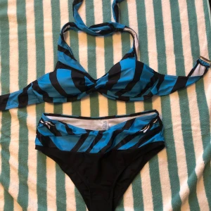 Blå och svart randig bikini - Snygg bikini i blått och svart med randigt mönster. Överdelen har en knytning i nacken och en twist-detalj framtill. Perfekt för sommarens badäventyr!