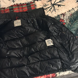 Svart dunjacka från Moncler - Säljer denna unika jackan från Moncler, jackan har fått en skavank på dragkedjan vilket moncler har problem med. Både knapparna har lossnat på dragkedjan. Cartoonet har också lossnat inuti. Jackan har funnits med ett tag o där med har inte jackan något kvitto. Jackan är i fint skick. Jag äger flera moncler jackor hemma så äktigheten kan ni va säkra på. Nypris är cirka 16 tusen.