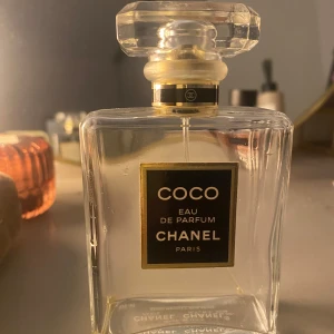 Coco Eau de Parfum från Chanel - Säljer en elegant flaska Coco Eau de Parfum från Chanel. Flaskan är fyrkantig och genomskinlig med en stilren svart och guld etikett. Flaskan har en lyxig känsla med sin kristalliknande kork. Passa på att köpa denna ikoniska parfymflaska!