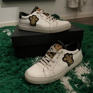Lords & Fools skor - Säljer ett par vita sneakers från Lords & Fools i bra skick. Skorna har snygga broderade detaljer i guld och svart på sidan och tungan. De är tillverkade i skinn och har en klassisk snörning. Perfekta för både vardag och fest! (Ny pris: 5500)