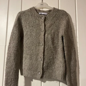 Beige/grå stickad kofta från ZARA - Superfin beige/grå stickad kofta från ZARA med glittriga pärldetaljer på kragen och knapparna. Passar både till vardags och fest!