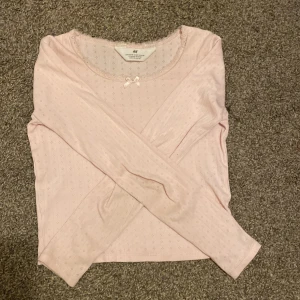 Ljusrosa långärmad topp från H&M - Säljer en söt ljusrosa långärmad topp från H&M. Den har ett diskret hålmönster och en fin liten rosett vid halsringningen. Perfekt för vår och sommar! 🌸