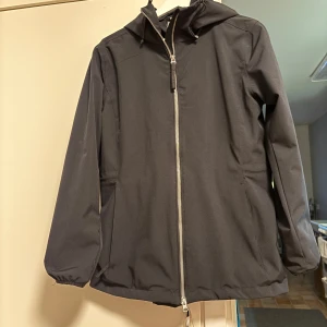 Svart vindjacka från McKinley - Säljer en svart vindjacka från McKinley med dragkedja och huva. Jackan har en stilren design och är perfekt för blåsiga dagar. Den är långärmad och har en normal passform.