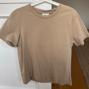 Beige t-shirt från GinaTricot  - Säljer en stilren beige t-shirt från GinaTricot. Den har en klassisk rund hals och korta ärmar. Materialet är bomull och går att både klä upp och ner🤎Skrynklig på bilden men går att stryka 
