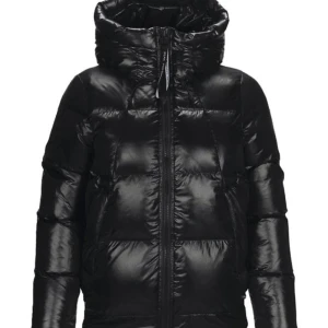 Svart pufferjacka med dragkedja - Snygg svart pufferjacka med hög krage och dragkedja framtill. Jackan har en glansig yta från peak performance 😇Den har långa ärmar och en bekväm passform.