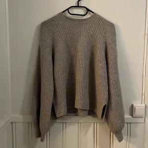 Beige stickad tröja från Weekday - Säljer en mysig beige stickad tröja från Weekday. Tröjan har en ribbad design och långa ärmar med en lös passform. Korta sprund i sidorna. Något nopprig. Perfekt för kyliga dagar!                    