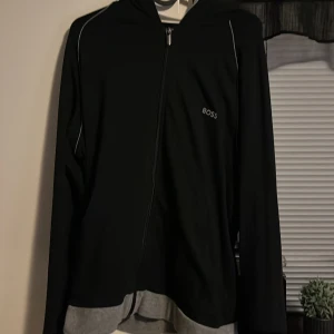 Svart kofta  från Boss - Snygg svart kofta  från Boss med dragkedja och diskret logga på bröstet. Perfekt för en stilren look.