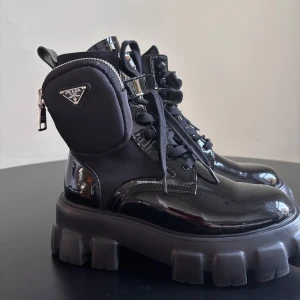 Prada monolith boots - Snygga svarta boots från Prada med hög platåsula och snörning. Skorna har en liten avtagbar ficka med dragkedja på sidan. Skorna är helt nya.