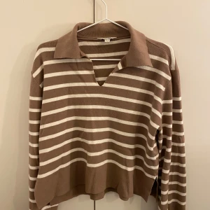 Brun och beige randig tröja - Säljer en brun och beige randig tröja med krage och v-ringning. Tröjan har långa ärmar och en avslappnad passform, perfekt för en bekväm stil.
