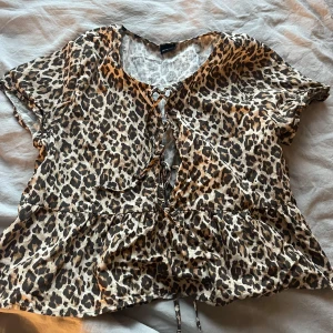 Leopardmönstrad blus från Gina Tricot - Säljer en leopardmönstrad blus från Gina Tricot med korta ärmar och knytning framtill. Blusen har en volangdetalj vid nederkanten som ger en fin form 