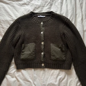 Brun stickad kofta från Zara - Säljer en grön stickad kofta från Zara med knappar framtill och två stora fickor. Koftan har en croppad passform och långa ärmar, perfekt för både vinter, vår och sommar. Den är både stilren och bekväm.💕💕