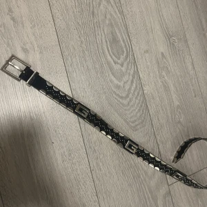 Svart bälte med silverdetaljer - Snyggt svart bälte med unika silverdetaljer och med silvriga ”G” plattor. CPerfekt för att ge en edgy touch till din outfit. Bältet har en rad med små silverkulor och halvcirkelformade detaljer längs hela längden. 92cm lång! 