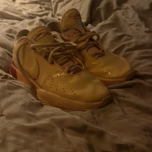 Gula sneakers med snörning - Snygga Lebron 21 dragon pearls med snörning och en unik sula. Skorna har en distinkt design med röda detaljer på hälen och perforeringar på sidorna för ventilation. De är i princip oanvända.